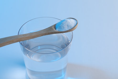 Glass of water and spoon with baking soda on light blue background, closeup. Space for textの写真素材