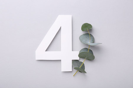 Paper number 4 and eucalyptus branch on light gray background, top view