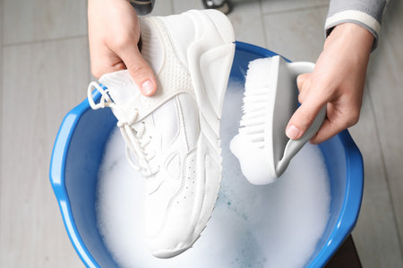 Woman cleaning stylish sneakers with brush in wash basin, top viewの写真素材
