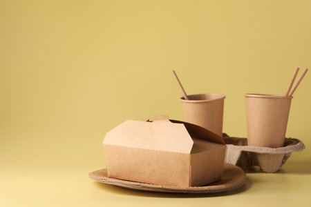 Eco friendly food packaging. Paper containers, cardboard cup holder and straws on pale yellow...