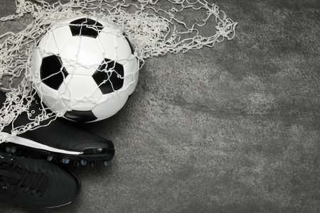 Sports equipment. Soccer ball, net and sneakers on gray textured table, flat lay. Space for text