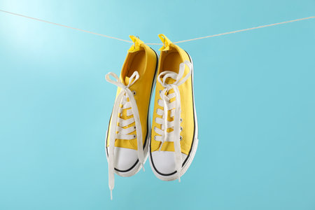Stylish sneakers drying on washing line against light blue backgroundの写真素材