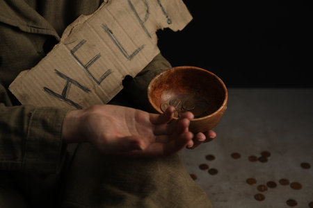 Poor homeless woman with help sign holding bowl of donations on floor, closeup