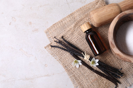 Vanilla pods, essential oil, flowers and sugar in bowl on light gray table, flat lay. Space for text