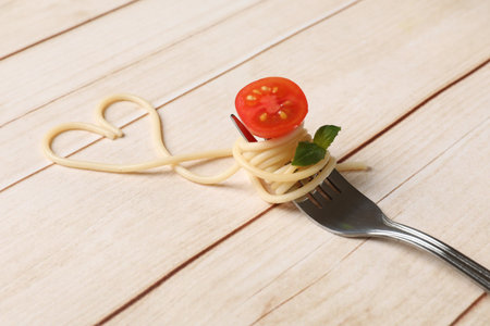 Heart made of tasty spaghetti, fork, tomato and basil on wooden table, closeupの写真素材