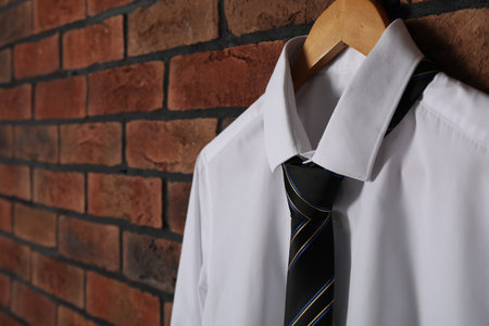 Hanger with white shirt and striped necktie on red brick wall, closeup. Space for textの写真素材