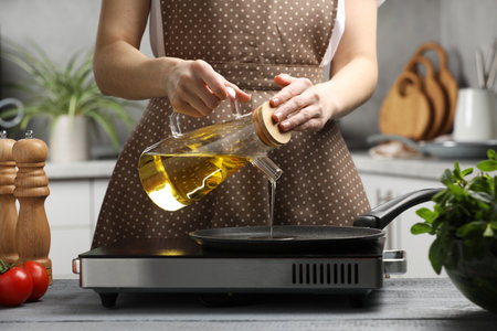 Vegetable fats. Woman pouring cooking oil into frying pan on stove in kitchen, closeupの写真素材