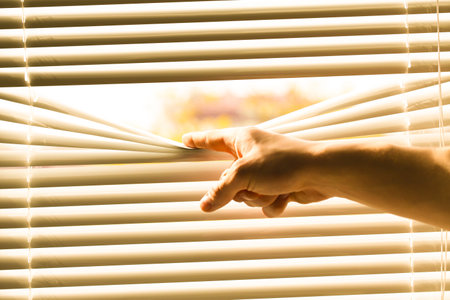 Man separating slats of white blinds indoors, closeupの写真素材