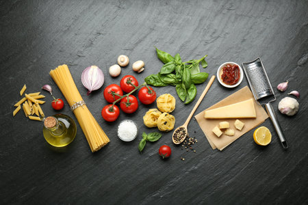 Different types of pasta, spices, garter and products on dark textured table, flat layの写真素材