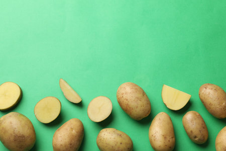 Fresh raw potatoes on green background, flat lay. Space for textの写真素材