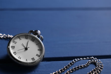 Silver pocket clock with chain on blue wooden table, closeup. Space for textの写真素材
