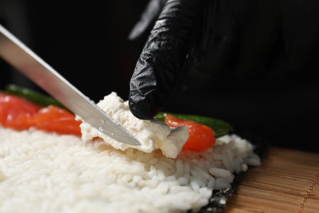 Chef in gloves putting cream cheese onto unwrapped sushi roll at table, closeupの写真素材