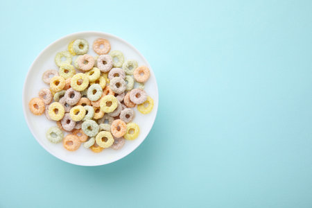 Tasty colorful cereal rings and milk in bowl on turquoise background, top view. Space for text