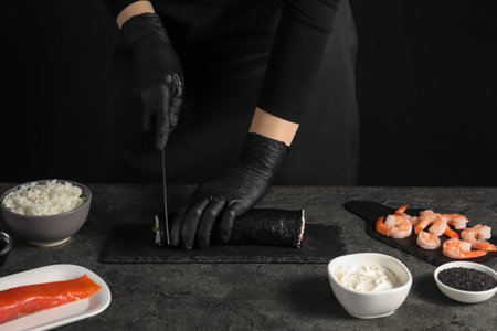 Chef in gloves cutting sushi roll at dark textured table, closeupの写真素材