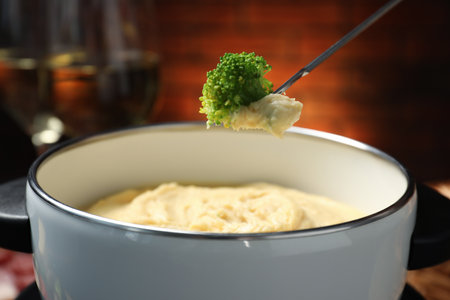 Dipping piece of broccoli into fondue pot with melted cheese on blurred background, closeupの写真素材