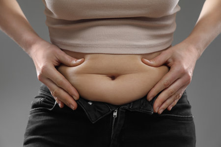 Woman touching belly fat on gray background, closeup. Overweight problemの写真素材