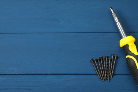 Screwdriver with black handle and screws on blue wooden table, flat lay. Space for text