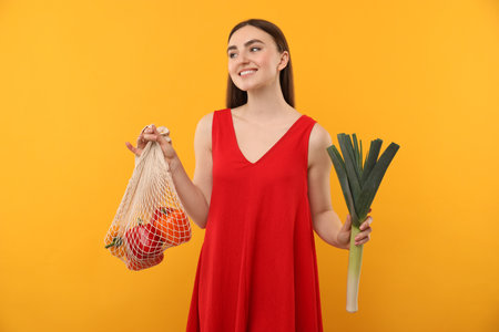Woman with string bag of fresh vegetables on orange backgroundの写真素材