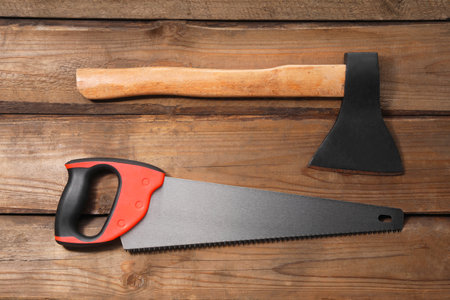 Saw with colorful handle and ax on wooden background, flat lay