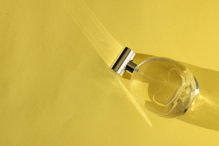 Luxury women's perfume. Sunlit glass bottle on yellow background, top view. Space for textの写真素材