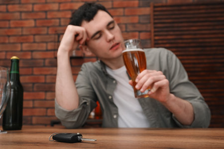 Man holding glass of alcoholic drink and sitting at table with car keys, selective focus. Don't drink and drive conceptの写真素材