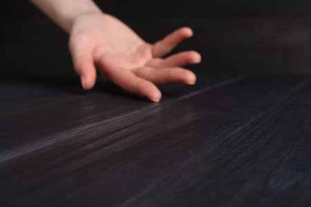 Woman holding hand above black wooden table, selective focus. Space for text