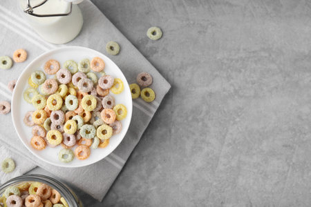 Tasty colorful cereal rings and milk in bowl on gray table, flat lay. Space for text