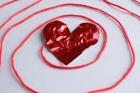 Red crumpled paper heart and thread on gray background, closeupの写真素材
