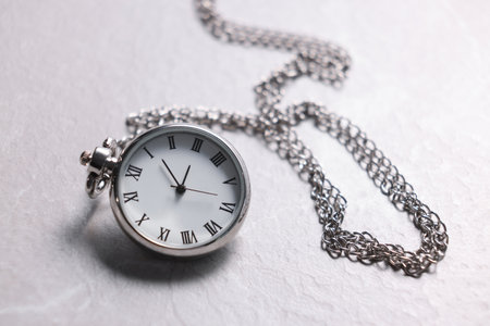 Silver pocket clock with chain on light textured table, closeup
