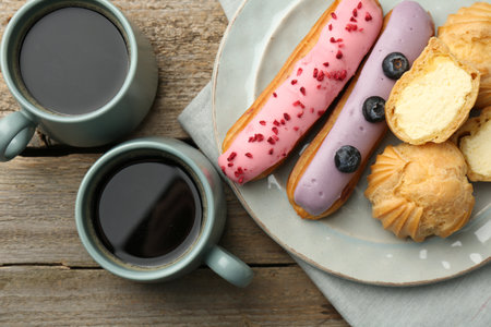 Aromatic coffee in cups, tasty eclairs and profiteroles on wooden table, top view