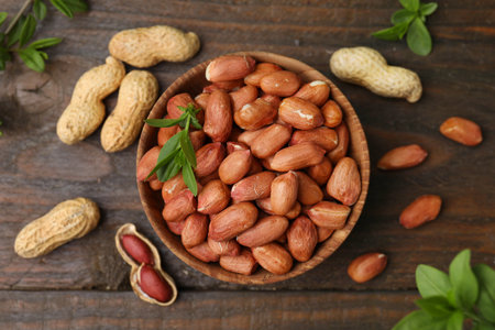 Fresh peanuts and leaves in bowl on wooden table, flat layの写真素材