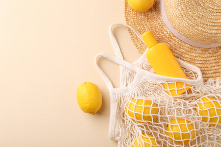 String bag with fresh lemons, sunscreen and straw hat on beige background, flat lay. Space for textの写真素材