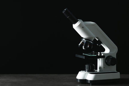 Modern microscope on gray table against black background, space for textの写真素材
