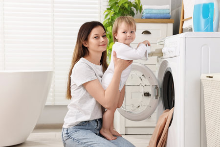 Mother with her daughter washing baby clothes in bathroomの写真素材