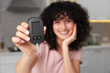 Diabetes. Happy woman holding digital glucometer in kitchen, selective focusの写真素材