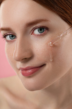 Beautiful woman with freckles applying cosmetic serum onto her face, closeup