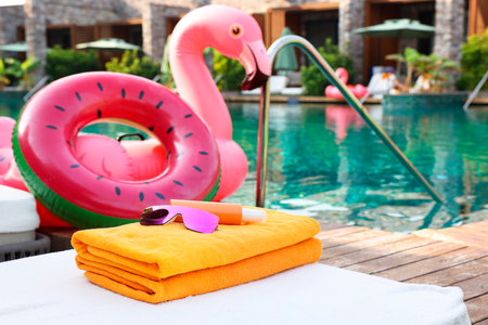 Beach accessories on sun lounger, inflatable ring and float near outdoor swimming pool at luxury resortの写真素材