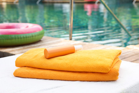 Beach towels and sunscreen on sun lounger near outdoor swimming pool, selective focus. Luxury resortの写真素材