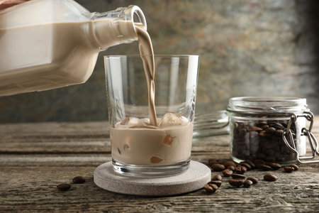 Pouring coffee cream liqueur into glass at wooden table, closeup