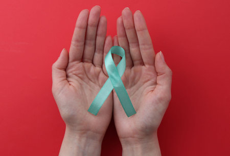 Woman holding turquoise awareness ribbon on red background, top viewの写真素材