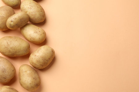 Fresh raw potatoes on pale orange background, flat lay. Space for textの写真素材