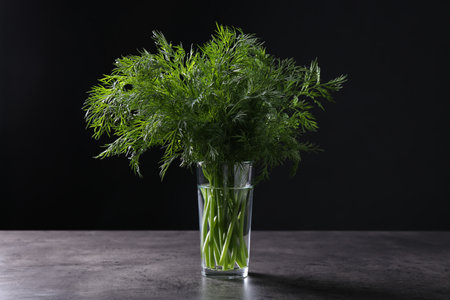 Fresh dill in glass on gray textured table against black background, closeupの写真素材