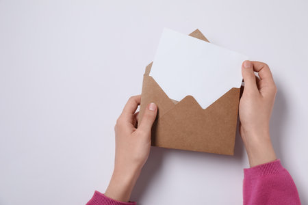 Woman taking card out of letter envelope at pink table, top view. Space for text