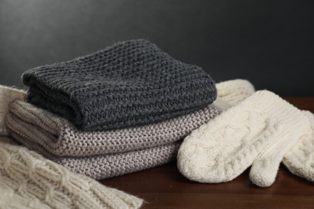 Knitted scarfs and mittens on wooden table against gray background, closeup