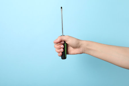 Woman holding screwdriver on light blue background, closeupの写真素材