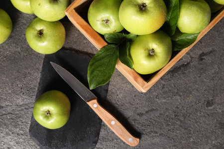Ripe green apples with water drops, cutting board and knife on gray table, flat layの写真素材