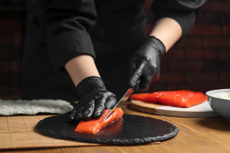 Chef in gloves cutting salmon for sushi at wooden table, closeupの写真素材