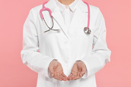 Doctor with stethoscope holding something on pink background, closeupの写真素材
