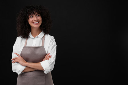 Happy woman wearing kitchen apron on black background, space for text. Mockup for designの写真素材