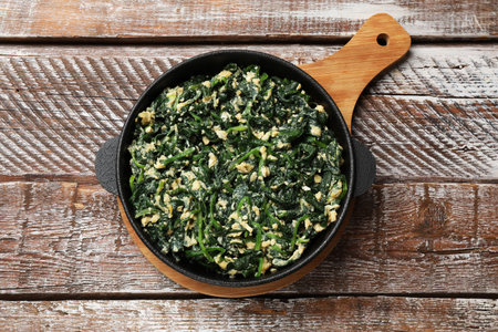 Tasty spinach dip with eggs in dish on wooden table, top view